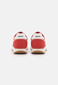 Baskets rouges avec une tige texturée, des accents blancs et un logo noir au talon. Elles disposent d'une semelle légère avec une adhérence à motif.