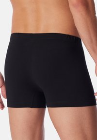 Boxer-briefs en coton noir avec une coupe ajustée, une taille élastique et sans motifs ni logos visibles. Texture lisse et design de jambe courte.