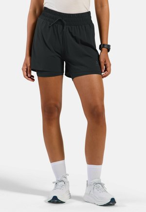 Person wearing black athletic shorts with inner lining, white socks, white running shoes, and a black smartwatch on left wrist.