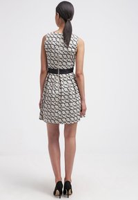 Robe sans manches à motif noir et blanc avec une taille cintrée, jupe évasée et détail de fermeture éclair à l'arrière ; associée à des talons hauts noirs.