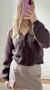 Σκούρο καφέ, υφασμένο πλεκτό κάρντιγκαν με V-λαιμόκοψη, μπροστά με κουμπιά και ριχτές μανσέτες, σε συνδυασμό με καρό φούστα που διαθέτει πλαϊνή σχισμή.