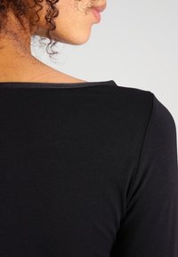 Maglietta nera maniche lunghe con scollatura ampia e rotonda e texture a coste, vista da dietro, che mette in evidenza il materiale e la vestibilità.