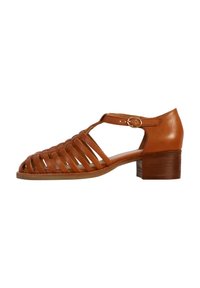 Tan leather sandal featuring a strappy design, open toe, and a low stacked heel. The shoe has an ankle strap with a circular metal buckle.
