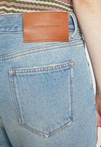 Ljusblå denimjeans med en brun läderetikett på bakfickan, med en enda bakficka och kontrasterande sömdetaljer.