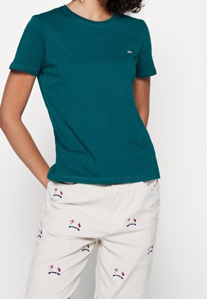 Turkooise katoenen T-shirt met een ronde hals, korte mouwen en een klein logo bij de borst, gecombineerd met crème kleurige ribfluwelen broek met geborduurde details.