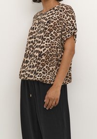 Haut à manches courtes en imprimé léopard beige et marron, avec une coupe décontractée et un col rond, associé à un pantalon fluide noir.