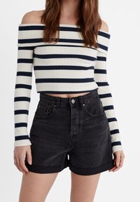 Off-the-shoulder ribbed top in white with navy stripes, paired with high-waisted black denim shorts featuring rolled cuffs and pockets.
