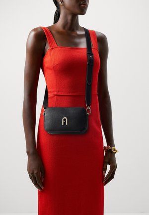 Borsa a tracolla in pelle nera con finitura testurizzata, dotata di logo dorato e elegante tracolla regolabile. Indossata con un vestito rosso.