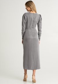 Abito grigio a maniche lunghe con spalle a sbuffo e una silhouette aderente, con scollo tondo e chiusura con zip sul retro. Tessuto liscio e leggero.