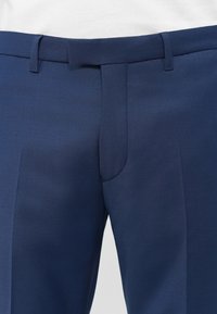 Blaue maßgeschneiderte Hose mit Gürtelschlaufen und verdecktem Reißverschluss, von der Taille bis zur Mitte des Oberschenkels auf einem weißen Hintergrund gezeigt.