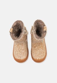 Bottines en textile marron à pois, avec une doublure intérieure douce, des semelles en caoutchouc et de petites languettes pour un enfilage facile. Détail de surface texturé marqué.