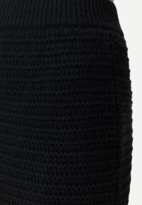 Närbild av svart stickat tyg med ribbad midjeresår och texturerat mönster på ett varmt plagg.