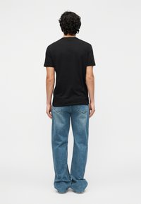 Čierne tričko s krátkym rukávom zobrazené zozadu, v kombinácii so svetlomodrými džínsami s rovnými nohavicami, na bielom pozadí.