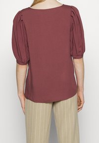 Bordowa bluzka z bufkami, okrągłym dekoltem i miękkim materiałem. Połączona z beżowymi spodniami w paski. Prosty i swobodny krój.