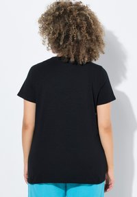 Černé tričko s krátkým rukávem a kulatým výstřihem, s uvolněným střihem a hladkou texturou, doplněné o světlé modré kalhoty.