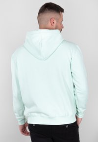 Felpa leggera di colore verde menta con tasca a marsupio, polsini e vita a costine. Presenta un cappuccio con lacci e una texture morbida e liscia.