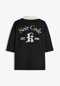 Zwarte polo met een witte kraag. Heeft "Noir Code" en "EST. 2001" in een contrasterend lettertype op de achterkant. Korte mouwen en een ontspannen pasvorm.