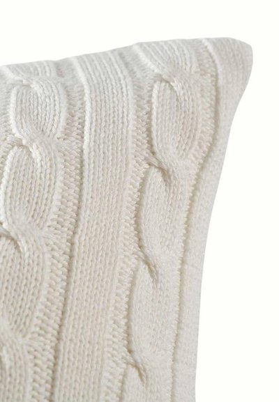 Κοντινό πλάνο ενός λευκού πλεκτού καλύμματος μαξιλαριού με κάθετα μοτίβα πλεξίδας και υφή ριμπ.