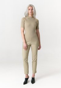 Beige geripptes Strickoberteil mit hohem Kragen und kurzen Ärmeln, kombiniert mit hellbeigen eng anliegenden Hosen und schwarzen offenen Sandaletten mit Absatz.