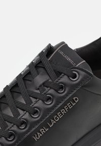 Zwarte leren sneakers met een gestructureerd oppervlak, ronde neus, platte veters, metalen oogjes en een geperst "KARL LAGERFELD" merknaam aan de zijkant.