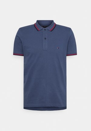 Polo bleu marine avec col rayé rouge et blanc, patte de boutonnage à deux boutons, manches courtes et petit logo brodé sur la poitrine.