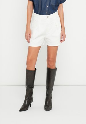 Valged kohandatud lühikesed püksid voldidega, kõrge vöökoha ja nööpidega, kombineeritud põlveni ulatuvate pruunide nahast kontsakingadega.