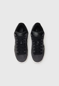 Čierne tenisky zo semišového materiálu s textúrovanými čiernymi detailmi, plochými šnúrkami a gumovou podrážkou. Vyznačujú sa minimalistickým dizajnom bez log.