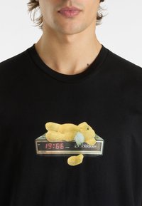 Black cotton T-shirt featuring a graphic of a yellow plush bear resting on a digital alarm clock displaying "19:66."