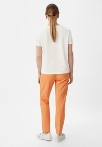 Weißes Baumwoll-T-Shirt mit kurzen Ärmeln, kombiniert mit schmal geschnittenen orangen Hosen und weißen Turnschuhen. Einfaches Design, keine Muster oder zusätzlichen Akzente.