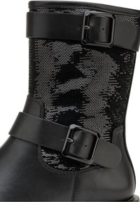 Botín negro con parte superior de cuero texturizado, panel de lentejuelas y dos correas ajustables negras con hebillas cuadradas.