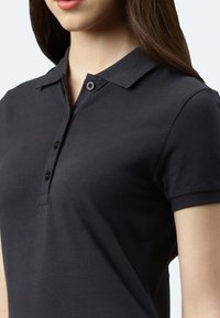Schwarzes Poloshirt mit klassischem Kragen, kurzen Ärmeln und einer zwei-knöpfigen Knopfleiste. Hergestellt aus strukturiertem Stoff, der eng am Körper anliegt.