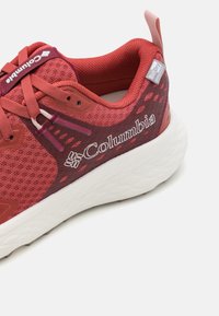 Rød mesh sneaker med en teksturert overdel, hvit polstret såle og en logo som leser "Columbia." Har kontrasterende snørebånd og forsterket hæl.