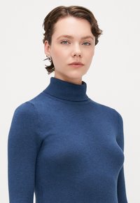 Μπλε, ριγωτό πουλόβερ με λαιμόκοψη, κατασκευασμένο από μαλακό ύφασμα, με εφαρμοστή σχεδίαση και μακρυά μανίκια, κατάλληλο για στρώσεις.