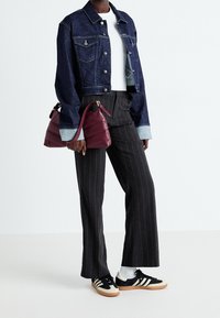 Jeansjacka i djupblått med kortad design, kombinerad med svarta smalrandiga byxor och svarta sneakers. Vinröd väska med texturerad yta.