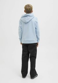 Felpa azzurra chiara con un grande cappuccio e polsini a coste, abbinata a pantaloni cargo neri con tasche laterali. Vista da dietro.