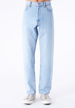 Jeans de mezclilla de tiro alto en azul claro con un corte recto, que cuentan con cinco bolsillos y un cierre de botón, combinados con zapatillas de lona beige.