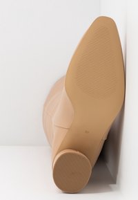 Beige ankle boot with a smooth texture, tapered toe, and a light-colored, ribbed rubber sole. Size 37 is marked on the sole.