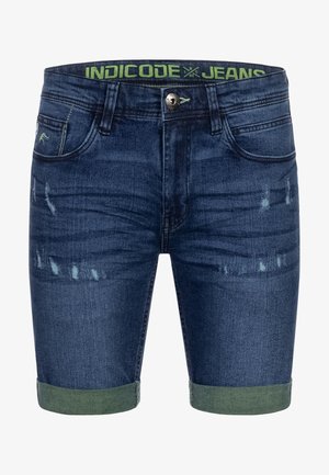 Dongeribukser i mørkeblått med slitte detaljer og rullede grønne mansjetter. Har knappelukking og merket midjebånd.