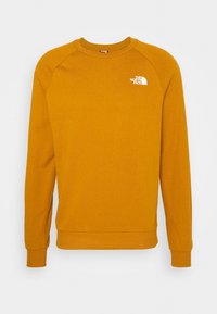 Sudadera de color mostaza con mangas largas, cuello y puños acanalados, presenta un pequeño logo blanco en el área del pecho izquierdo.