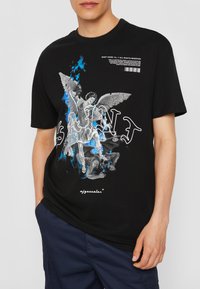 Schwarzes Baumwoll-T-Shirt mit einem zentralen Grafikmotiv eines Engels mit Flügeln und blauen Flammendetails, mit fettem "SAINT"-Text und Markenlogo.