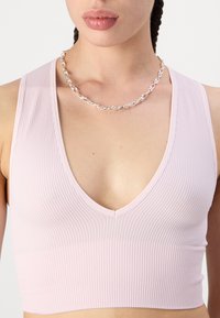 Svijetloružasti rebrasti crop top s dubokim V-izrezom i glatkom teksturom, uparен s srebrnom lančićem.