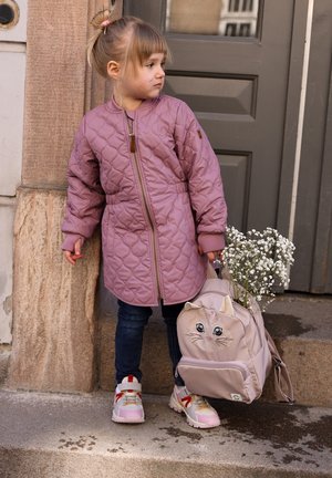 Roosa tikandiga jakk lukuga, sinised teksapüksid ja valged tossud. Beež seljakott kassi näo disainiga, hoides valgeid lilli.