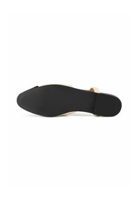 Scarpa a suola piatta con suola in gomma nera e parte superiore beige chiaro. Presenta un design minimalista con una fascia che attraversa il piede.