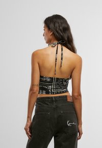 Mustmust mustriipudega halter-top, millel on kinnitamine selja taga. Mudel kombineerib selle tumedate teksadega, millel on logo seljal.