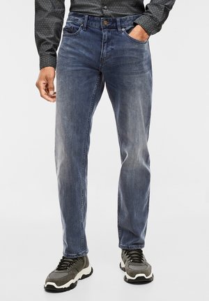 Dark blue denim jeans with a straight-leg design, featuring light fading and subtle stitching details. Paired with grey athletic shoes.
