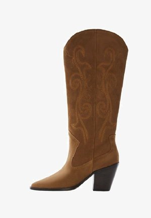 Bota de vaquero de ante marrón con punta afilada y tacón alto. Presenta bordados en forma de remolinos en un tono más claro que resaltan el diseño.