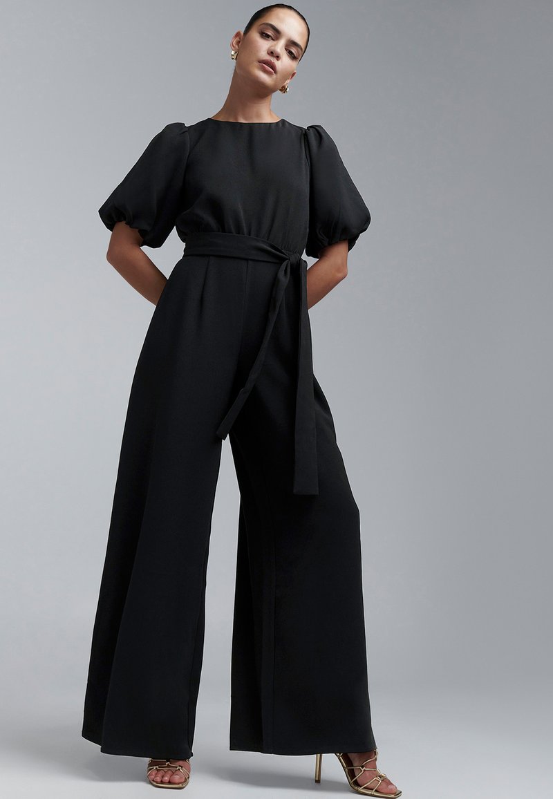 Zwarte jumpsuit met pofmouwen, brede pijpen en een strikceintuur. Gemaakt van soepel stof, met een ronde halslijn en een minimalistisch ontwerp.