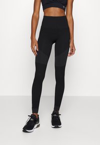 Leggings negros de cintura alta con paneles texturizados, presentan un diseño ajustado y acentos de puntos en la parte inferior de las piernas. El material parece elástico.