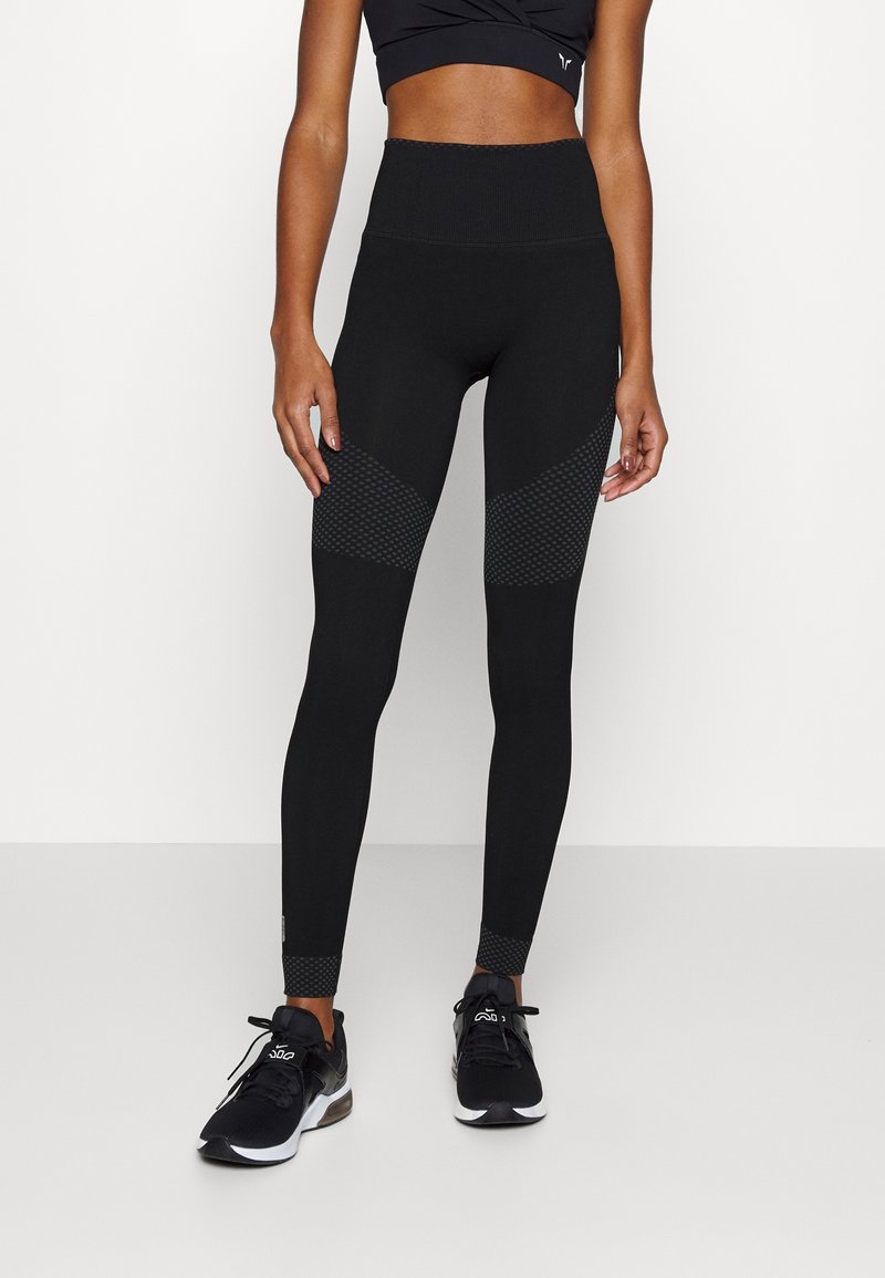 Leggings negros de cintura alta con paneles texturizados, presentan un diseño ajustado y acentos de puntos en la parte inferior de las piernas. El material parece elástico.