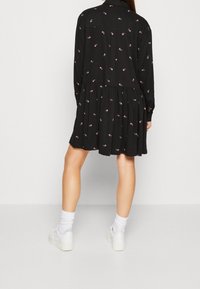 Svart klänning med lång ärm, mönstrad med små rosa blommor, med en knapp-up krage och en stjärtkjol.